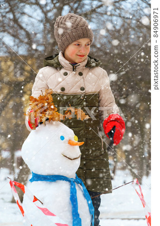 a girl plays with snow on a city street and makes a snowman 84906971