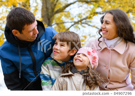 Portrait of a happy family in an autumn park. People pose against the background of beautiful yellow trees. They hug and are happy together. 84907296