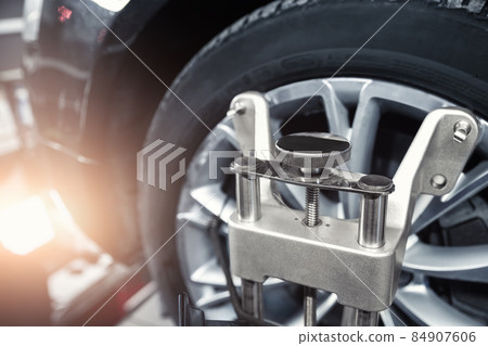 CLose-up car wheel indoors service maintenance repair center against laser sensor equipment diagnostics and 3d wheel alignment. Vehicle inside garage workshop for auto camber toe check fixing work 84907606