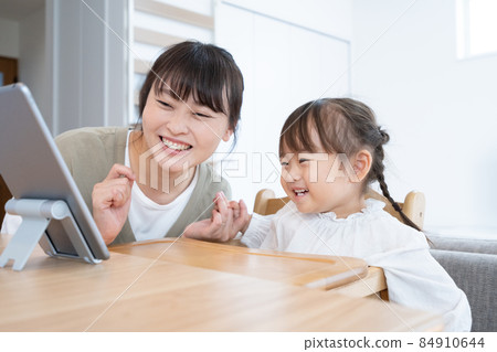 A 2-year-old girl looking at a tablet with her mom in the dining room at home 84910644