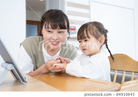 一個 2 歲的女孩和媽媽在家裡的餐廳裡看平板電腦 84910645