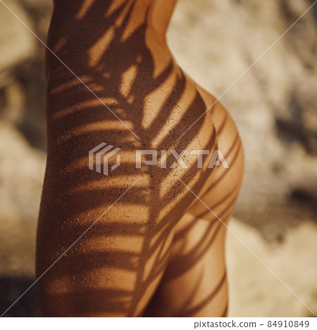 Close-up Woman's Tanned Naked Buttocks Under the Palm Leaf Shade on the Deserted Beach Outdoors Close-up Woman's Tanned Naked Buttocks Under the Palm Leaf Shade on the Deserted Beach Outdoors 84910849