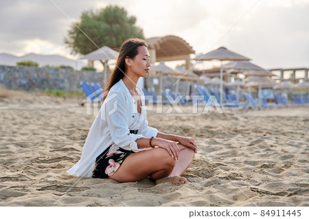 Young relaxed woman sitting in lotus position on beach, morning sea nature 84911445