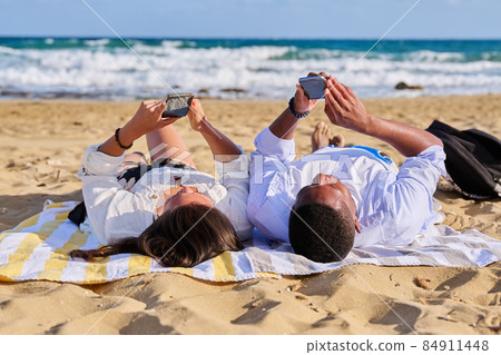 Young multicultural couple lying on the beach using smartphones 84911448