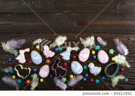 Cookie cutters feathers and Easter frosted cookies in shape of egg, chicken and rabbit on dark wooden background. Flat lay with copy space. Cookie cutters feathers and Easter frosted cookies in shape of egg, chicken and rabbit on dark wooden background. Flat lay with copy space. 84912992