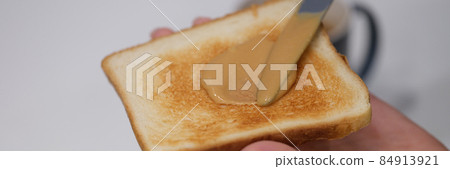 Woman spreads peanut butter on toast with knife closeup 84913921