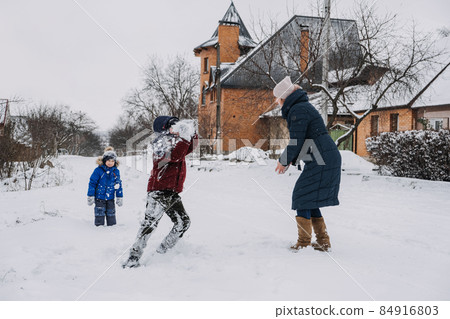 Outdoor family activities for happy winter holidays. Happy mother and two sons playing snowballs on snowy street in suburb. Happy family on winter weekend, Christmas holidays Outdoor family activities for happy winter holidays. Happy mother and two sons playing snowballs on snowy street in suburb. Happy family on winter weekend, Christmas holidays 84916803