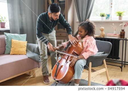 Young man bending over cute diligent schoolgirl with cello 84917894