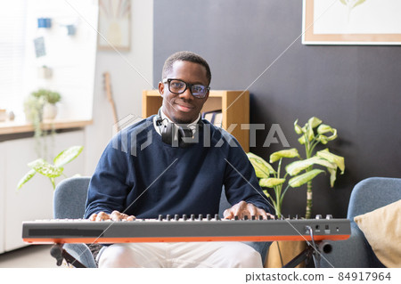 Happy young man in eyeglasses and casualwear sitting by piano keyboard 84917964