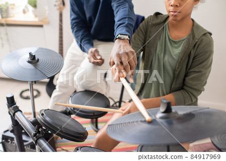 African male teacher explaining schoolgirl how to play drumkit 84917969