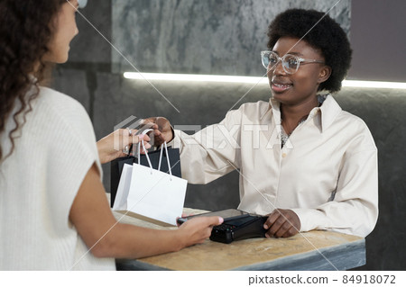 Happy young African female passing consumer paperbags with purchased goods Happy young African female passing consumer paperbags with purchased goods 84918072