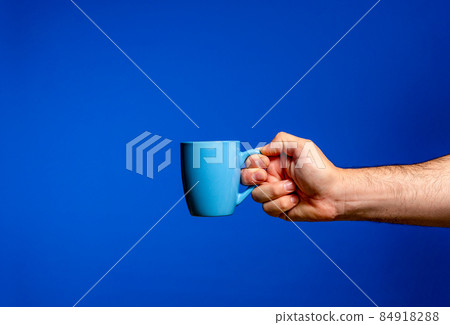 Man's hand holding a blue cup of coffee isolated on blue background. The cup contains an exquisite coffee with an intense aroma 84918288