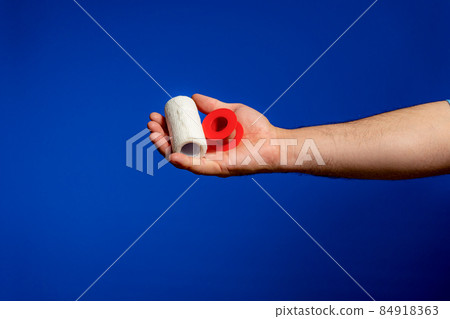 Man's hand offering on his palm a bandage and a roll of tape. Basic equipment for any wound. Isolated on blue studio background Man's hand offering on his palm a bandage and a roll of tape. Basic equipment for any wound. Isolated on blue studio background 84918363