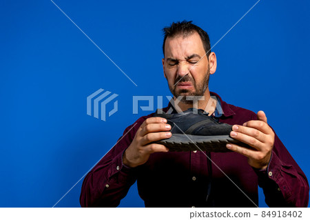 A man hold sneaker in his hands. Nasty smell. Stink legs, fungus on the legs. A man hold sneaker in his hands. Nasty smell. Stink legs, fungus on the legs. 84918402