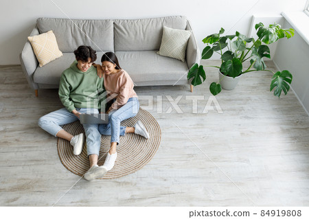 Young Asian couple using laptop, surfing internet or watching movie online, sitting on floor in living room, top view Young Asian couple using laptop, surfing internet or watching movie online, sitting on floor in living room, top view 84919808