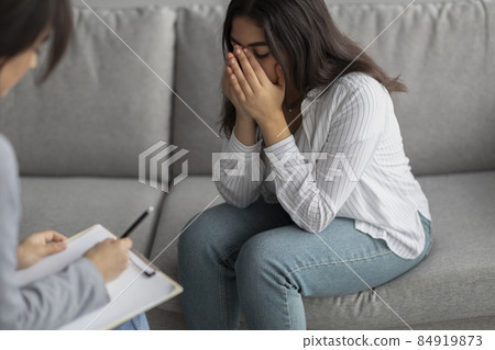 Despaired arab lady sitting on sofa, crying, taking to psychologist in clinic, suffering from depression, stress Despaired arab lady sitting on sofa, crying, taking to psychologist in clinic, suffering from depression, stress 84919873