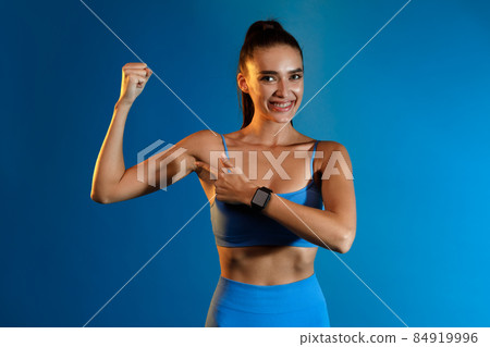 Fitness Lady Pointing Finger At Biceps Standing Over Blue Background Fitness Lady Pointing Finger At Biceps Standing Over Blue Background 84919996
