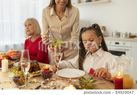 Millennial woman putting vegetable salad on her daughter's plate during Christmas dinner with family at home Millennial woman putting vegetable salad on her daughter's plate during Christmas dinner with family at home 84920047