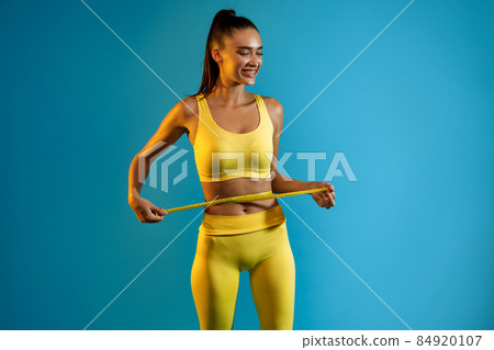 Fit Woman Measuring Waist With Tape After Weight-Loss, Blue Background Fit Woman Measuring Waist With Tape After Weight-Loss, Blue Background 84920107