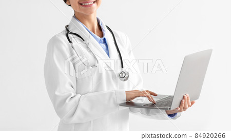 Cropped young indian lady doctor in white coat with stethoscope typing on computer on light background Cropped young indian lady doctor in white coat with stethoscope typing on computer on light background 84920266