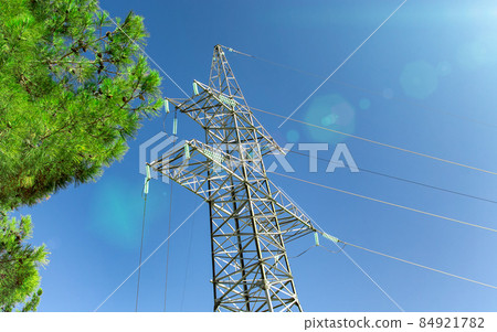High-voltage transmission pylon against a blue sky, sun and green branches. Green energy concept. 84921782
