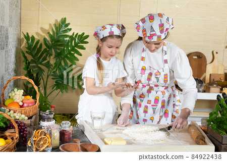 Mum stirs the dough with a kitchen knife and her five-year-old daughter does it with a spoon. Mother and baby do the dough together in the kitchen. 84922438