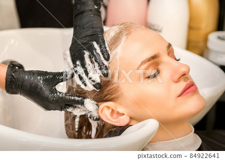 Young caucasian blonde woman having hair washed in the sink at a beauty salon. 84922641