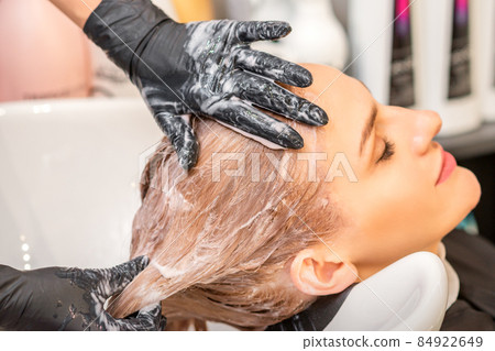 Young caucasian blonde woman having hair washed in the sink at a beauty salon. 84922649