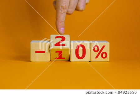 Hand turns a cube and changes the expression '-10 percent' to '-20 percent'. Beautiful orange background, copy space. Business concept. Hand turns a cube and changes the expression '-10 percent' to '-20 percent'. Beautiful orange background, copy space. Business concept. 84923550