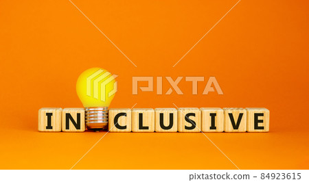 Symbol for a better inclusion. Wooden cubes with word 'inclusive'. Yellow light bulb. Beautiful orange background. Copy space. 84923615