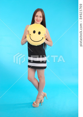 Cheerful young girl is holding a smiley face pillow Cheerful young girl is holding a smiley face pillow 84923769