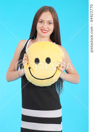 Cheerful young girl is holding a smiley face pillow Cheerful young girl is holding a smiley face pillow 84923770