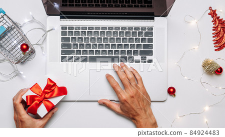Holiday online shopping. Gift box red ribbon, trolley and laptop, money in flat lay internet shopping composition. Merry Christmas and Happy New Year. Holiday online shopping. Gift box red ribbon, trolley and laptop, money in flat lay internet shopping composition. Merry Christmas and Happy New Year. 84924483