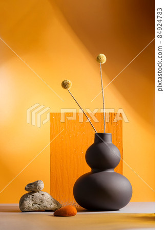 Dry yellow flowers on a trend black vase on orange background with orange glass 84924783