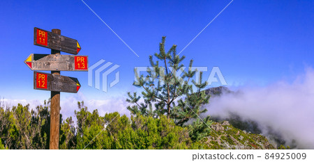 Hiking activity in Madeira island rocky mountains. Direction signs for Pico Ruivo highest point passing in the clouds Hiking activity in Madeira island rocky mountains. Direction signs for Pico Ruivo highest point passing in the clouds 84925009