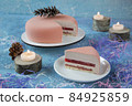 Round pink strawberry Christmas cake and piece of cake with cones surrounded by burning candles and decorations for Christmas is a delicious dessert for celebrating the holiday 84925859