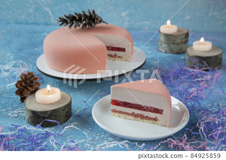 Round pink strawberry Christmas cake and piece of cake with cones surrounded by burning candles and decorations for Christmas is a delicious dessert for celebrating the holiday Round pink strawberry Christmas cake and piece of cake with cones surrounded by burning candles and decorations for Christmas is a delicious dessert for celebrating the holiday 84925859
