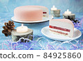 A beautiful pink festive New Year's cake for Christmas with candles and a cut piece on a plate. Cones, tinsel and sawn wood are used for decoration 84925860