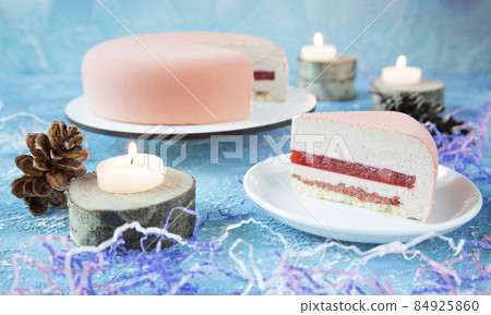 A beautiful pink festive New Year's cake for Christmas with candles and a cut piece on a plate. Cones, tinsel and sawn wood are used for decoration A beautiful pink festive New Year's cake for Christmas with candles and a cut piece on a plate. Cones, tinsel and sawn wood are used for decoration 84925860