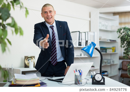 Positive European man office manager reaching out his hand for handshake and looking in camera. 84929776