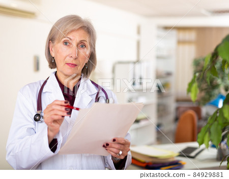 Elderly female doctor with papers studying clinical diagnosis of patient Elderly female doctor with papers studying clinical diagnosis of patient 84929881