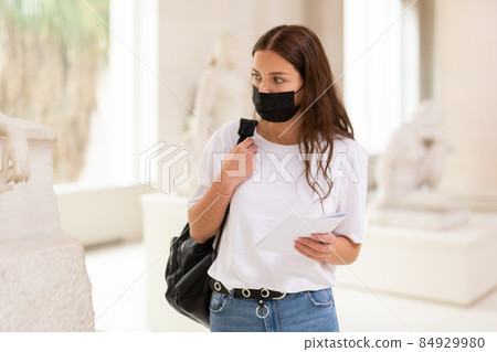 Focused girl in a protective mask in the museum looks at the sculpture 84929980