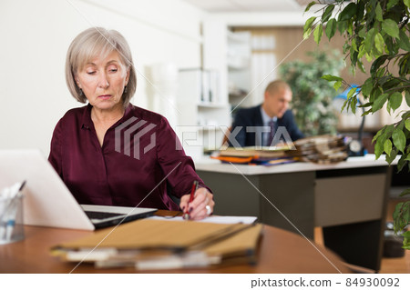 Busy focused aged female entrepreneur working with papers and laptop 84930092