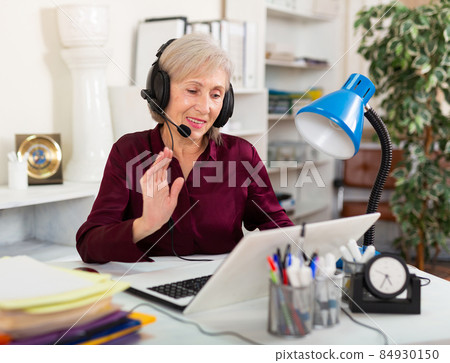 Elderly businesswoman in headphones holding video meeting with customer 84930150
