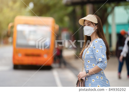 woman with medical mask to protect coronavirus(covid-19) while waiting bus at bus stop in city 84930202