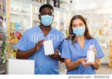 Portrait of two pharmacists in protective masks, demonstrating goods in a pharmacy Portrait of two pharmacists in protective masks, demonstrating goods in a pharmacy 84930219