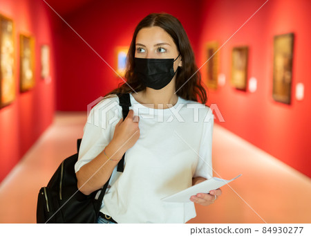 Young girl in a protective mask visits an exhibition of paintings in a museum 84930277
