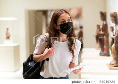 Young girl wearing a protective mask in the museum looks at the exhibits 84930289