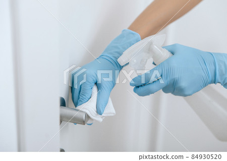 Cleaning black door handle with an antiseptic wet wipe, blue gloves and sanitizer. Sanitize surfaces prevention in hospital and public spaces against corona virus. Woman hand using towel for cleaning. Cleaning black door handle with an antiseptic wet wipe, blue gloves and sanitizer. Sanitize surfaces prevention in hospital and public spaces against corona virus. Woman hand using towel for cleaning. 84930520