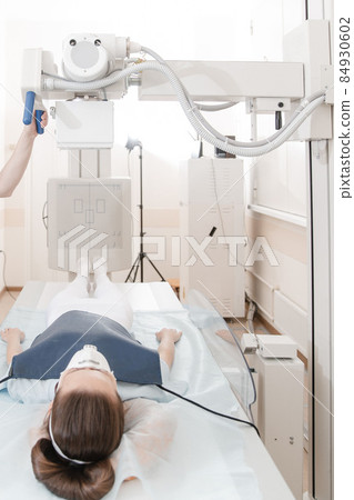 Doctor taking x-ray of patient lying on gurney. Hospital radiology room. Technician adjusting an x-ray machine. Female lying on a bed is scanning chest, heart, lungs in modern clinic office. 84930602